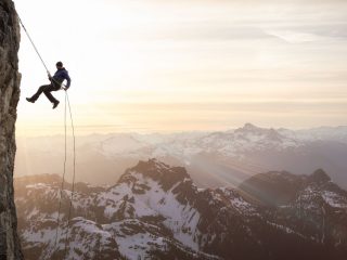A person climbing the cliff with a rope with views of mountains tops